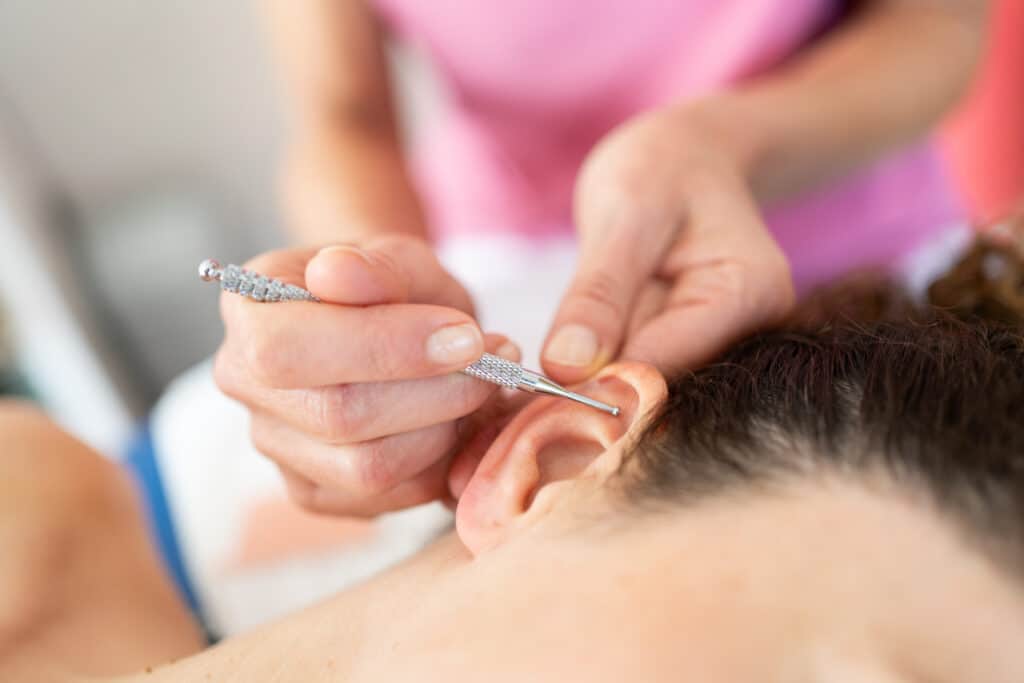 Auriculothérapie : Soulagement et bien-être par l'oreille Main tenant un outil métallique stimulant l'oreille d'une personne, vue rapprochée d'une séance d'auriculothérapie professionnelle.