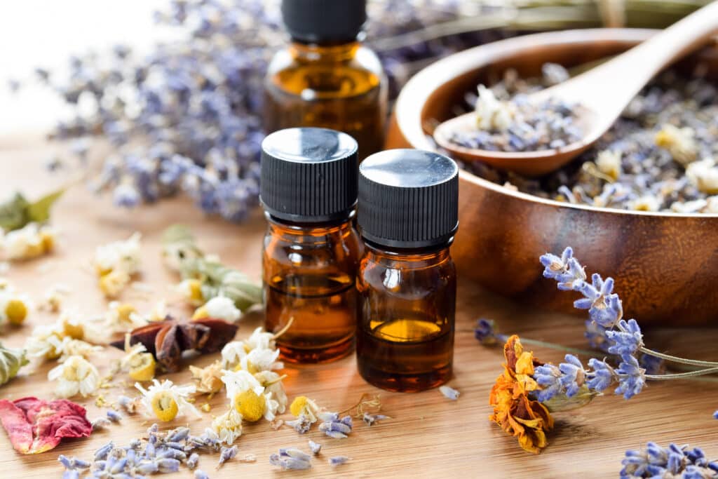Bouteilles d'huiles essentielles avec lavande, camomille et herbes séchées sur bois, évoquant l'aromathérapie et le bien-être.