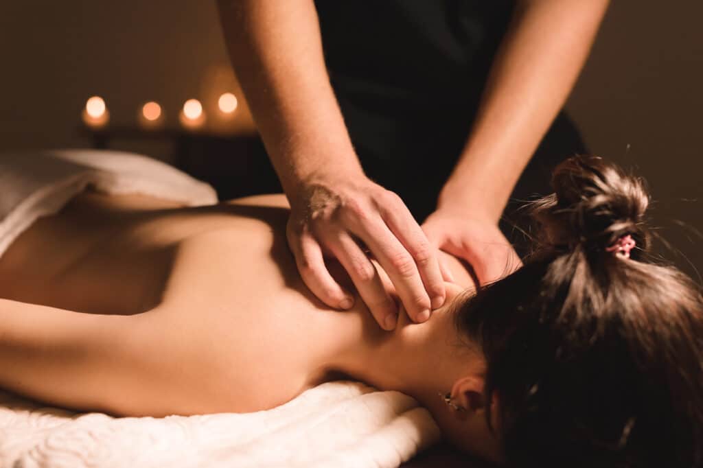 Massage relaxant: Desserrez les tensions du cou et du dos. Femme recevant un massage du cou et du dos par un masseur. Ambiance tamisée relaxante avec lumières douces.