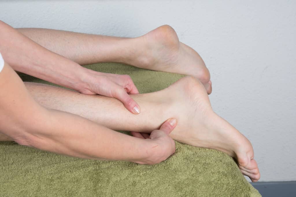 Massage thérapeutique jambe et cheville | Soulagement. Mains massant la jambe et la cheville d'une personne allongée sur serviette verte, traitement de physiothérapie.