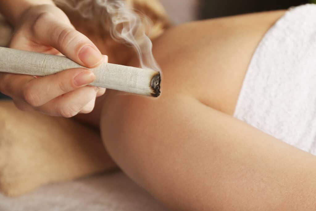 Moxibustion : Soin ancestral pour votre bien-être Main tenant un bâton de moxa allumé produisant de la fumée blanche près du bras d'une personne pour une séance de moxibustion.