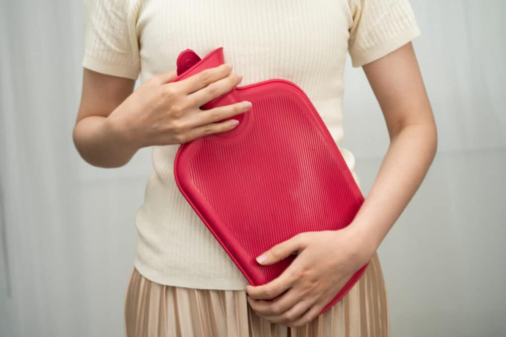 Bouillotte rouge pour soulager les douleurs abdominales et crampes Femme tenant une bouillotte rouge sur son ventre, cherchant le soulagement de douleurs abdominales ou menstruelles.
