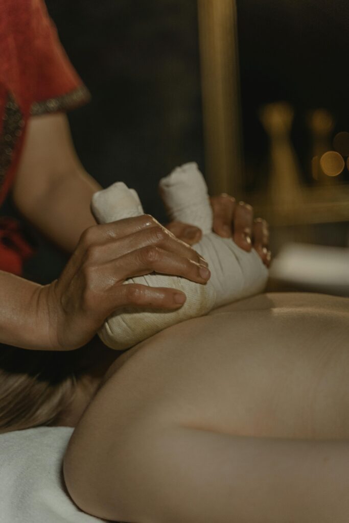 Massage aux pochons chauds thaïlandais : relaxation profonde Mains d'une masseuse utilisant des pochons chauds de massage thaïlandais sur le dos nu d'une personne allongée, ambiance tamisée.